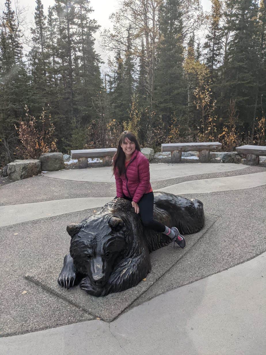 Jami sitting on a statue of a sleeping bear in front of Denali National Park's Visitor Center