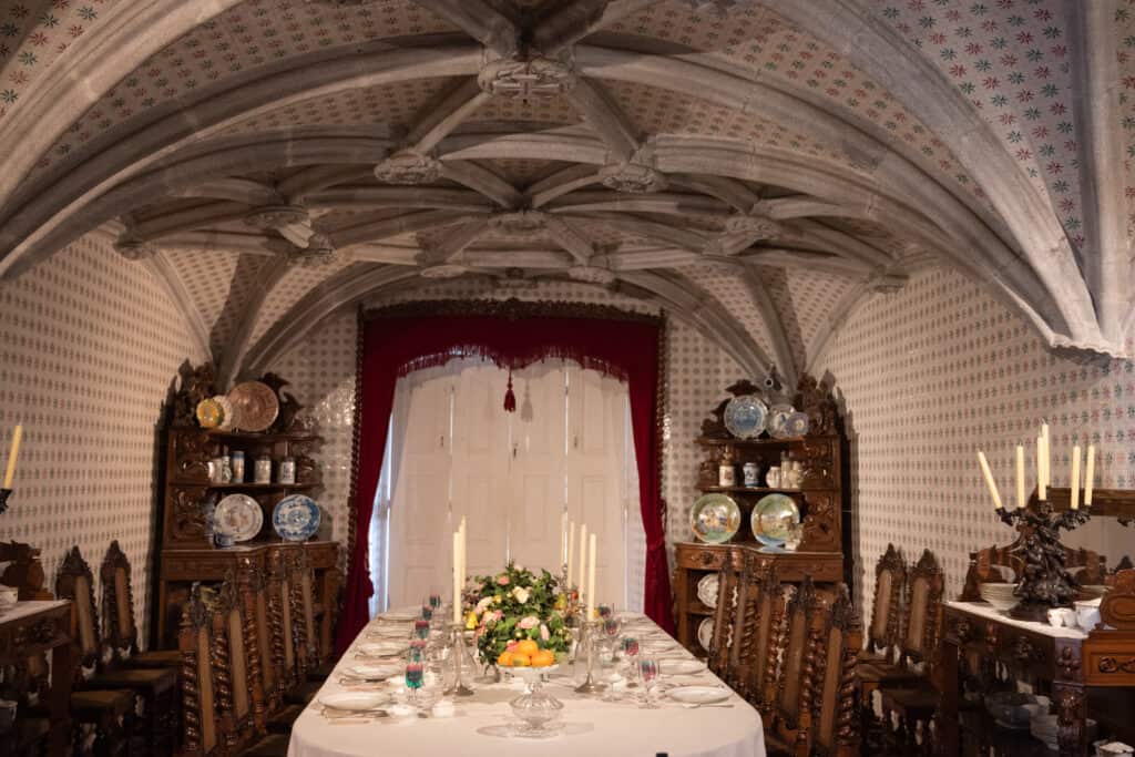 Buttressed ceiling with red and blue details. A large set dinner table in the small room.