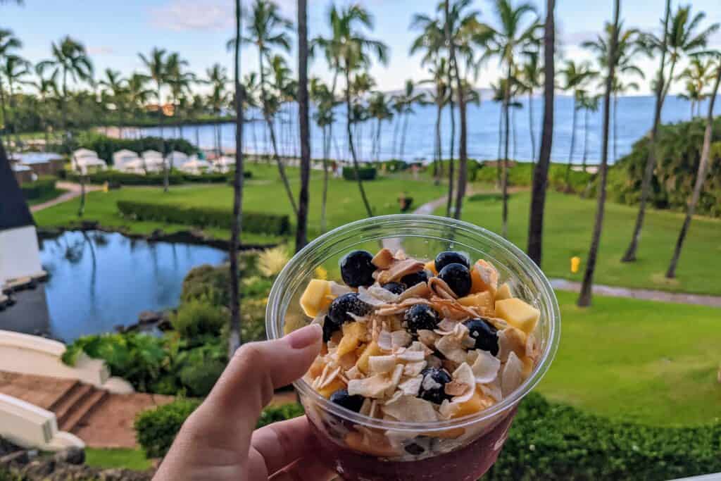 Blueberries, Coconut, and Mango In an açaí bowl with Hawaiian palm trees and ocean in the background