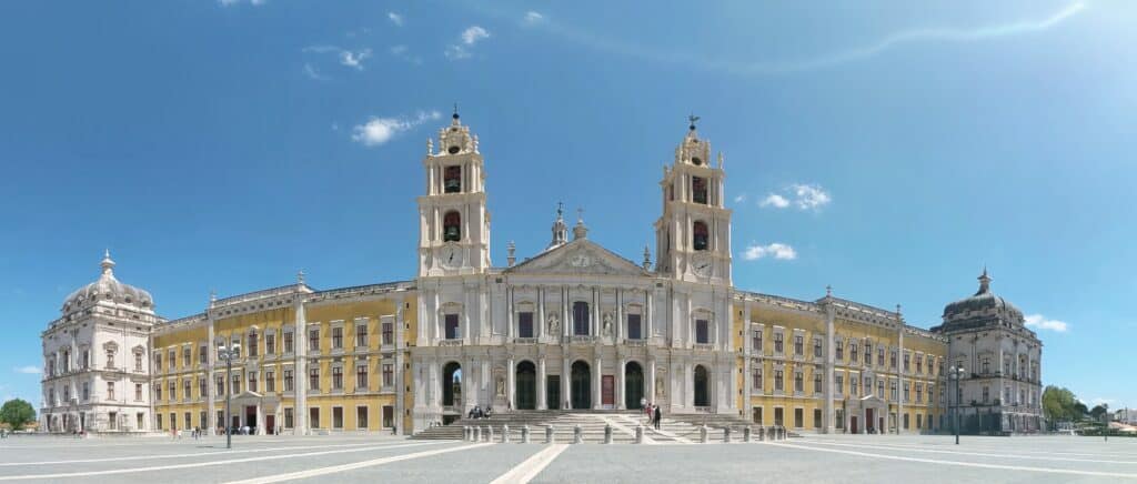 White basilica with two bell towers and a yellow wing of Mafra palace on either side.