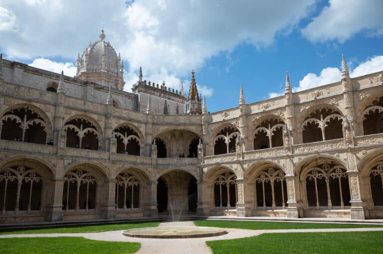 the interior of the cloister in the monastery. Green grass with a building on the outside. 2 levels of decorative arches on the