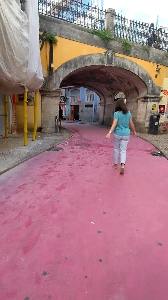 Street painted pink with grey cobblestones and a yellow bridge in Lisbon