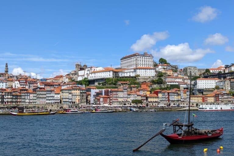 A red boat on the water with Porto rising from riverside in the background.