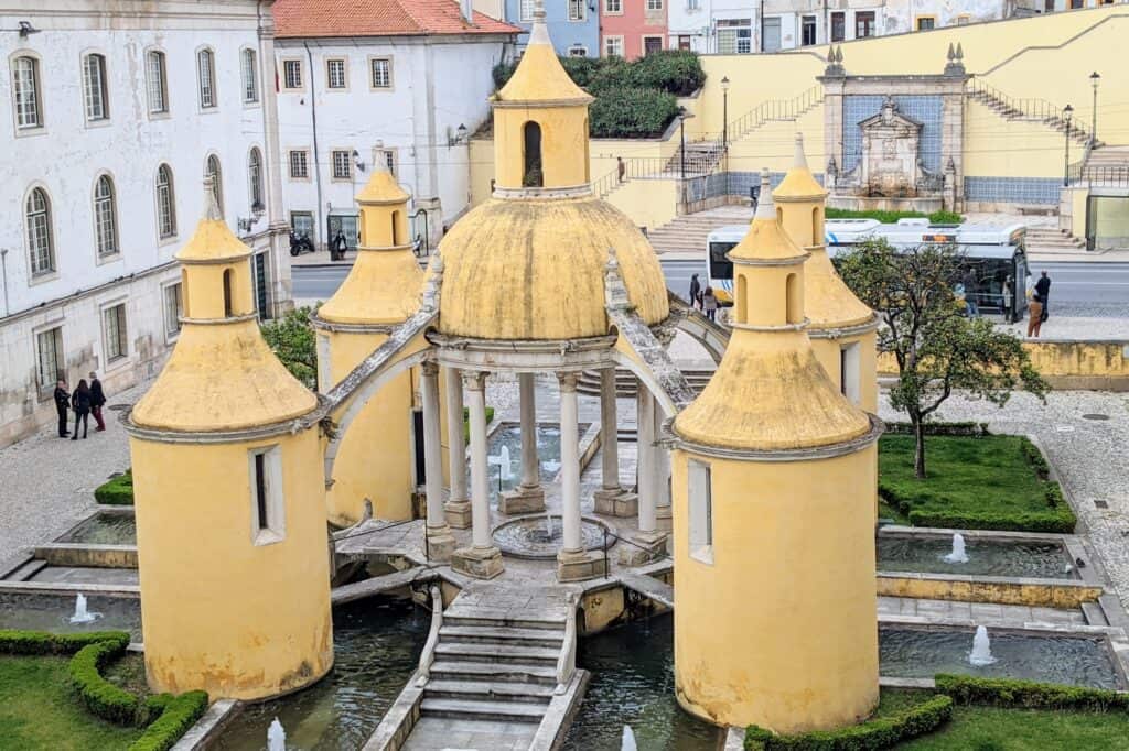 Yellow monument in coimbra. 4 yellow columns surround an inner fountain with a yellow dome above.