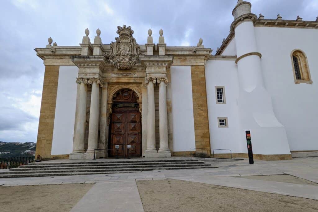 Exterior of library in Coimbra. White facade with brown stone and light brown columns.