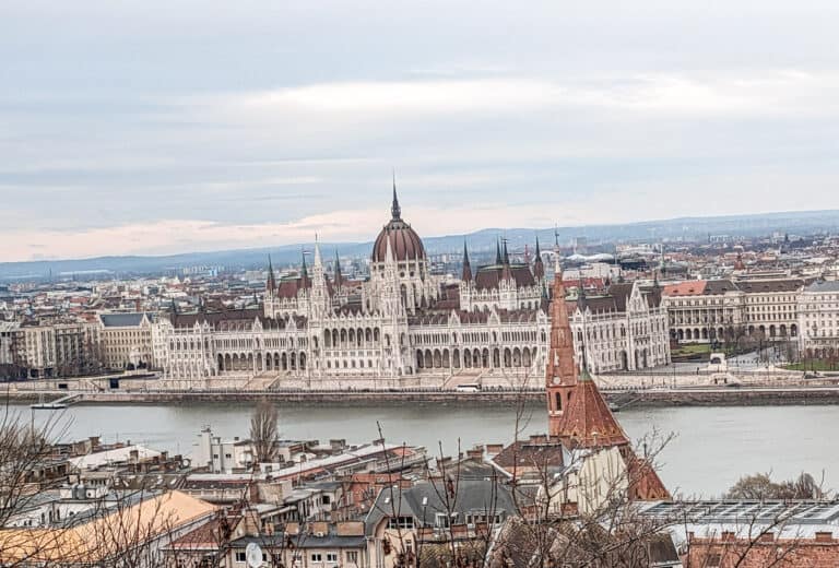 View of Hungarian Parliament from Buda Hill. The white gothic building with it's red rooftops sits on the water.