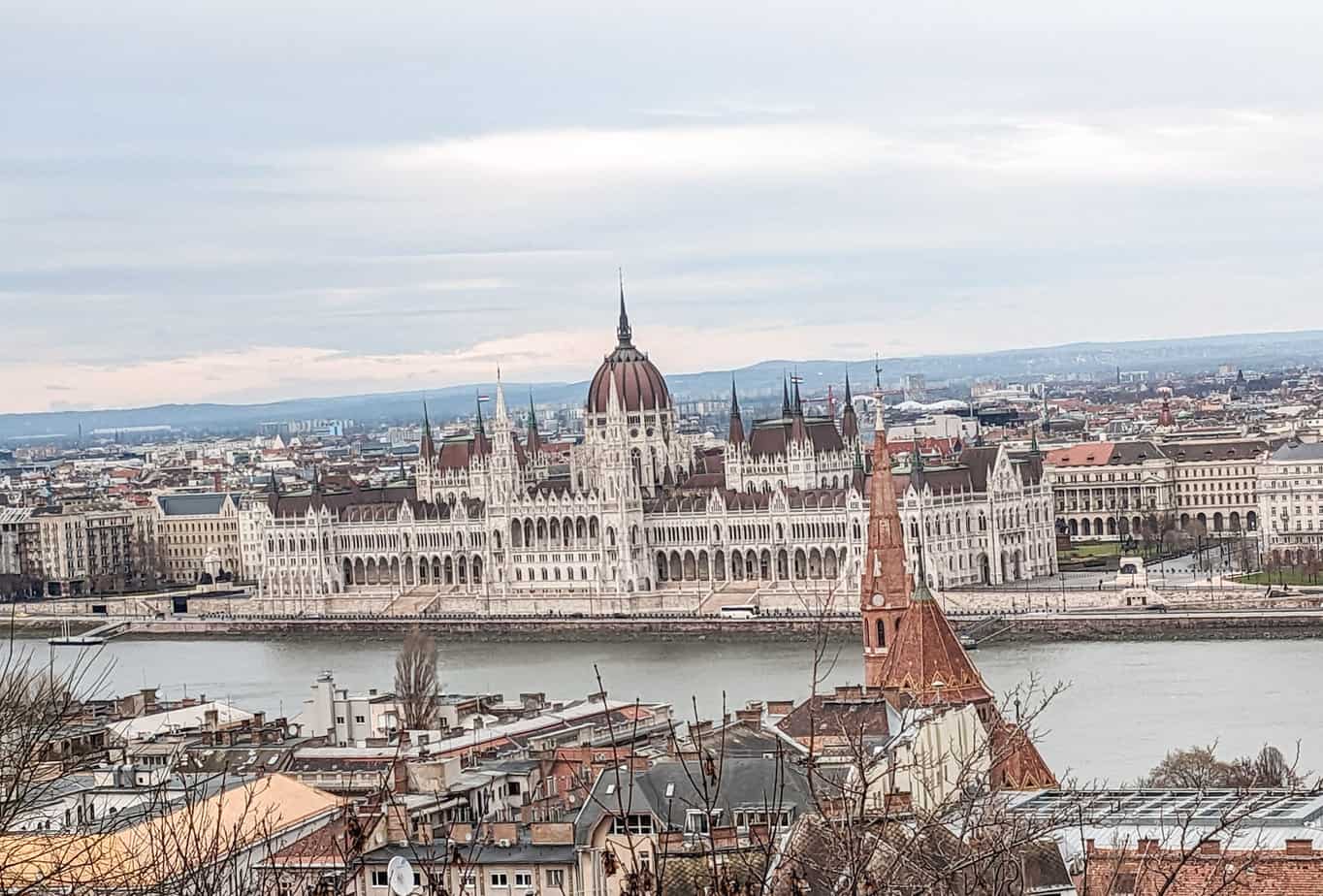 View of Hungarian Parliament from Buda Hill. The white gothic building with it's red rooftops sits on the water.