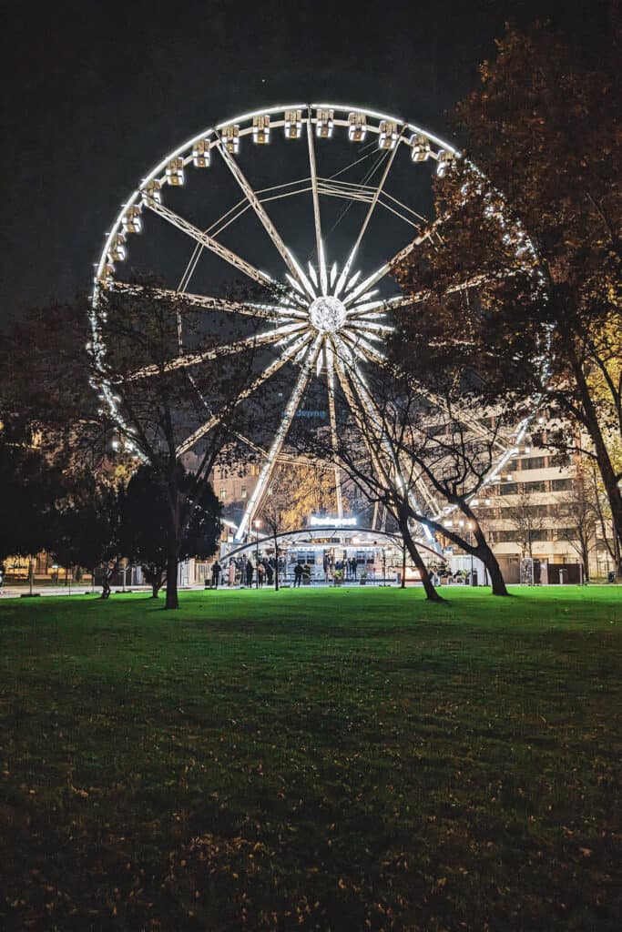 Budapest Eye in Erezbet Square at night with lights making it bright. People wait in line to get on.