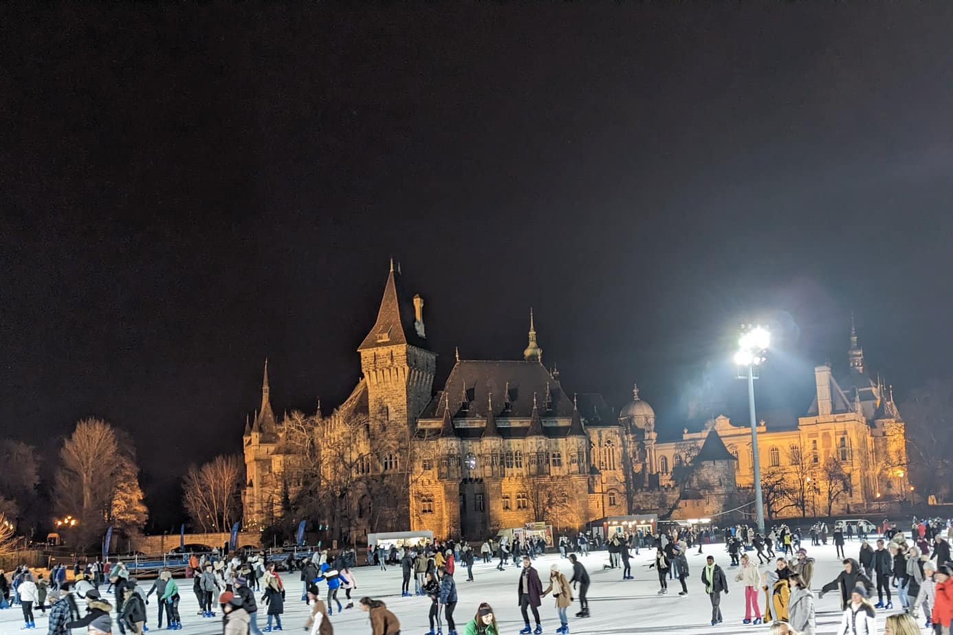 Vajdahunyad Castle with skating rink at night. People skating on the ice under the lights.