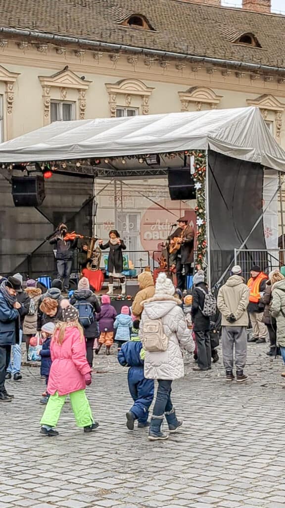 View of a performance on a small stage at Obuda Christmas market. Families and children are in front of teh stage dancing
