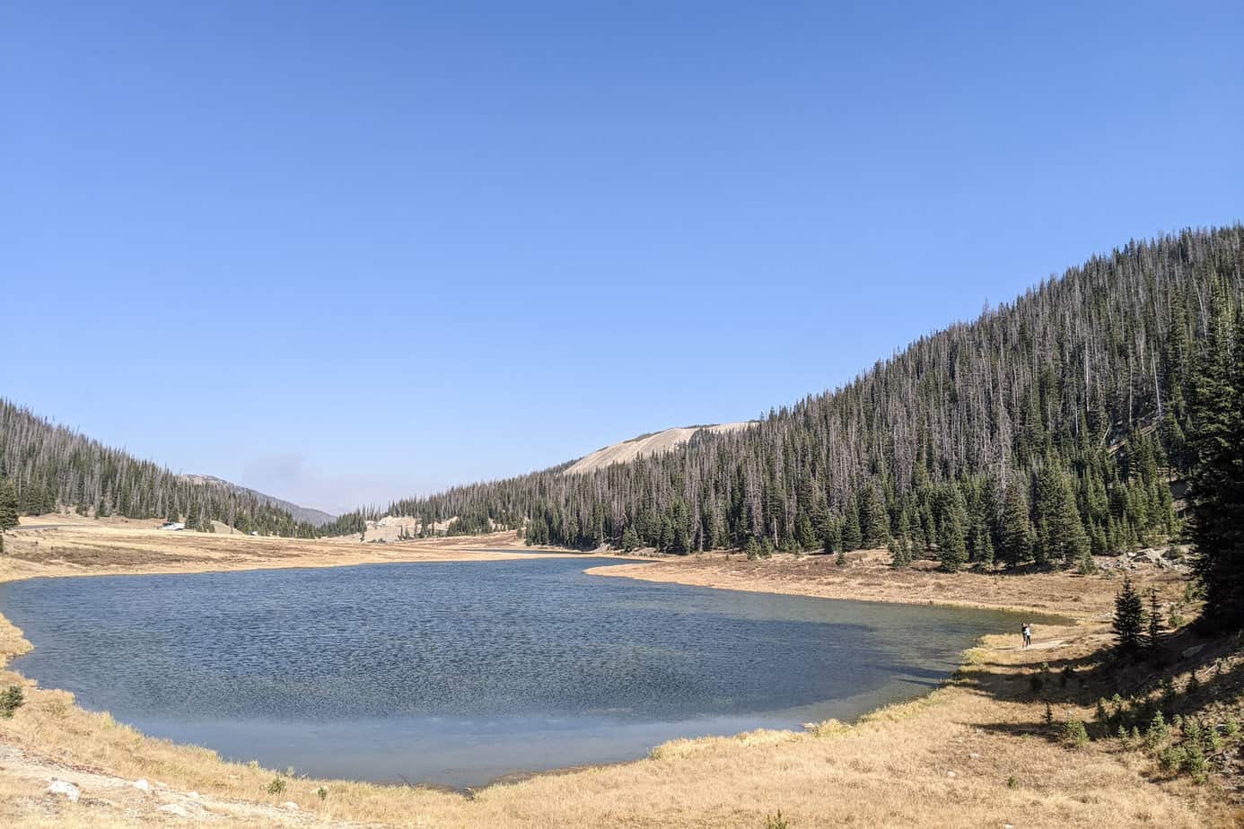 an alpine lake with a path around it. Trees line the hills to the side.