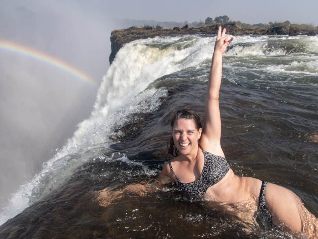 Jami at the edge of Victoria Falls in Devil's Pool with a rainbow in the background