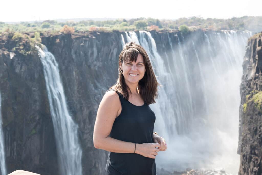 Jami stands in a black tank top in front of Victoria Falls